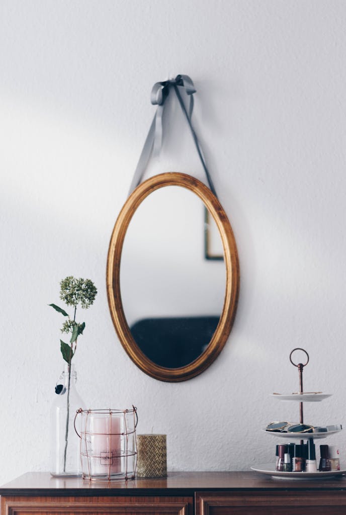 A stylish interior setup featuring a hanging oval mirror with decorative elements on a wooden table.